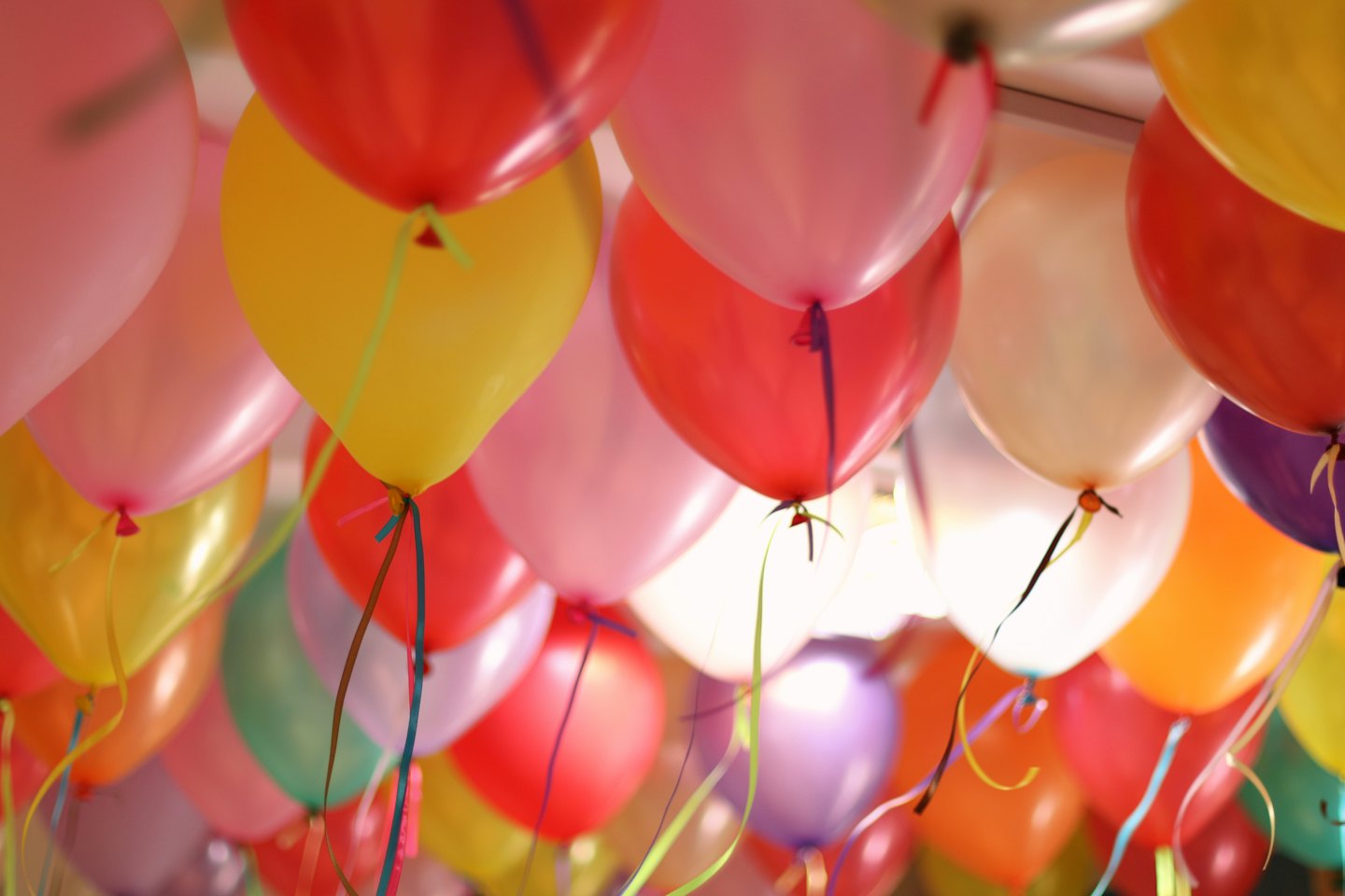 Colorful helium balloons floating indoors against a ceiling.