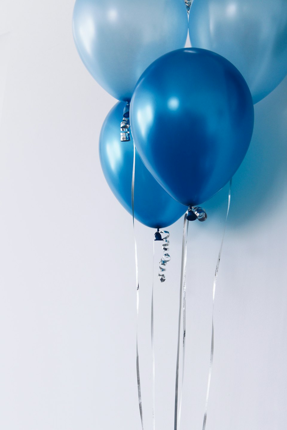 Clusters of blue balloons tied with silver ribbons float upward.