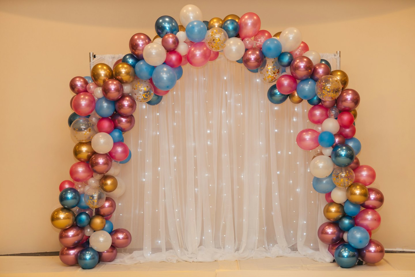 Pink, blue, gold, and white balloon arch with fairy lights.